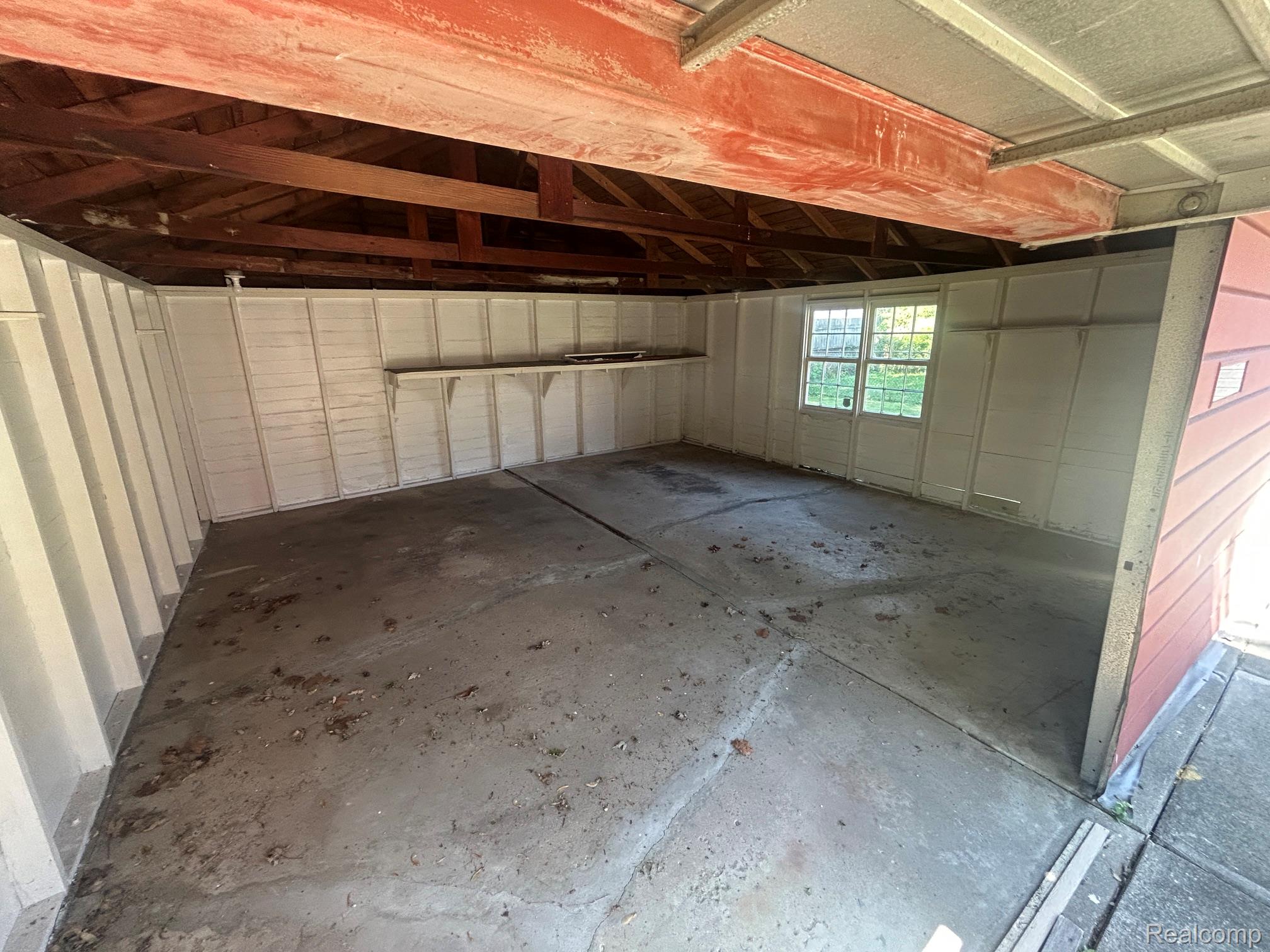 21970 Moross Road Grosse Pointe, MI 48236 - Photo 20 of 21 Concrete floor garage with exposed wood rafters, white paneled walls, a built-in storage shelf, and a double-hung window