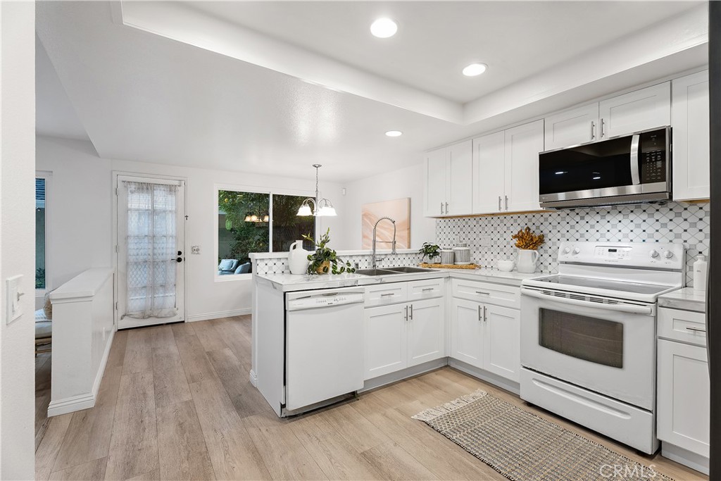 16 East Yale Loop, Unit 28 Irvine, CA 92604 - Photo 8 of 44 a kitchen with stainless steel appliances granite countertop a stove top oven a sink dishwasher and white cabinets with wooden floor
