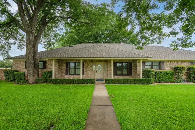 a view of a brick house with a big yard and large trees