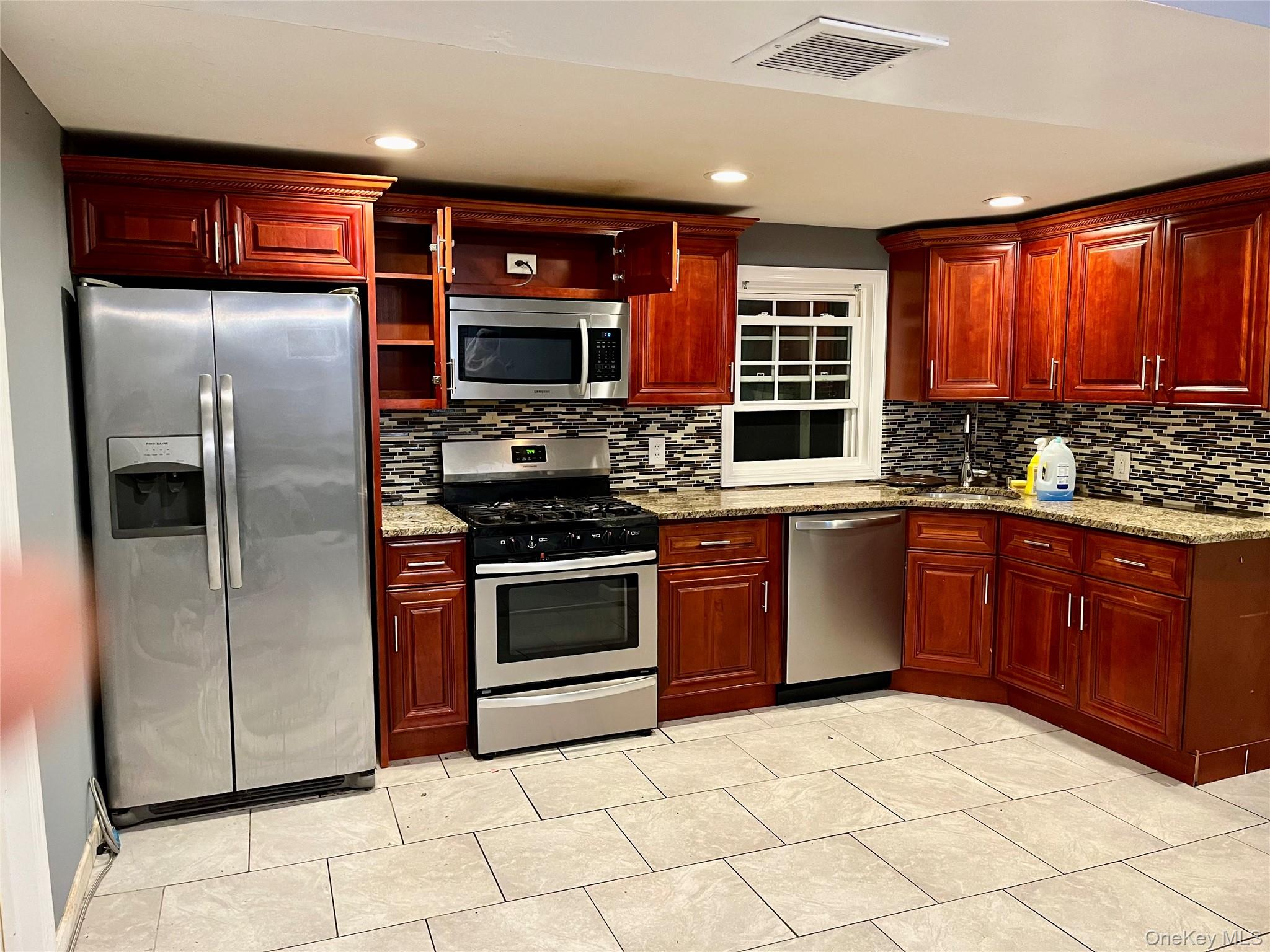 47 College Road Selden, NY 11784 - Photo 2 of 15 Kitchen with reddish brown cabinets, stainless steel appliances, light stone countertops, recessed lighting, and light tile patterned floors