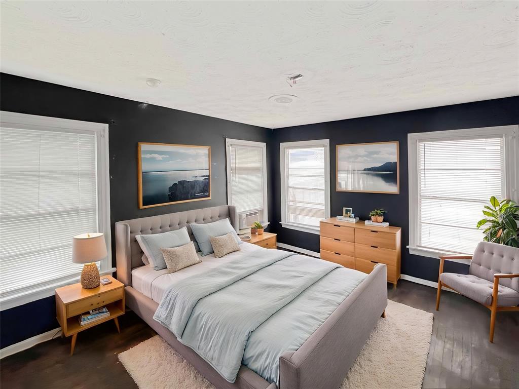 1010 Winters Street Dallas, TX 75216 - Photo 3 of 20 Bedroom featuring four windows with blinds, dark wall paint, wood-finish flooring, and a ceiling-mounted light fixture