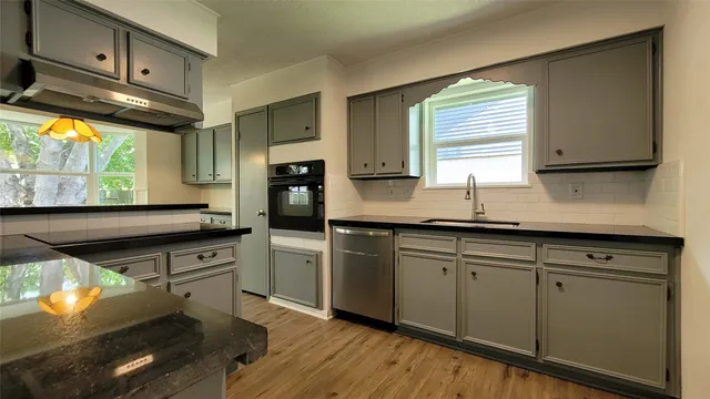 a kitchen with stainless steel appliances granite countertop a sink a stove a refrigerator cabinets and a large window