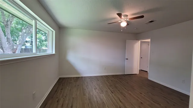 an empty room with wooden floor fan and windows