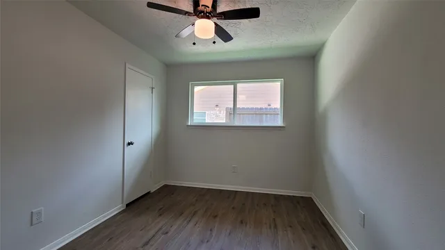 an empty room with wooden floor ceiling fan and windows
