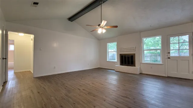 an empty room with wooden floor a ceiling fan a fireplace and windows in a room
