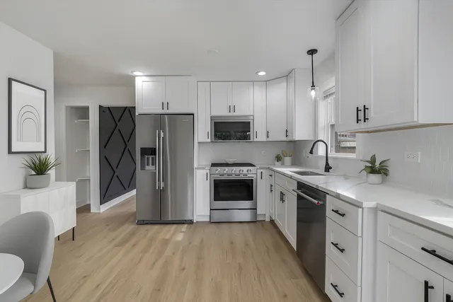 a kitchen with granite countertop a refrigerator oven a sink dishwasher and white cabinets with wooden floor