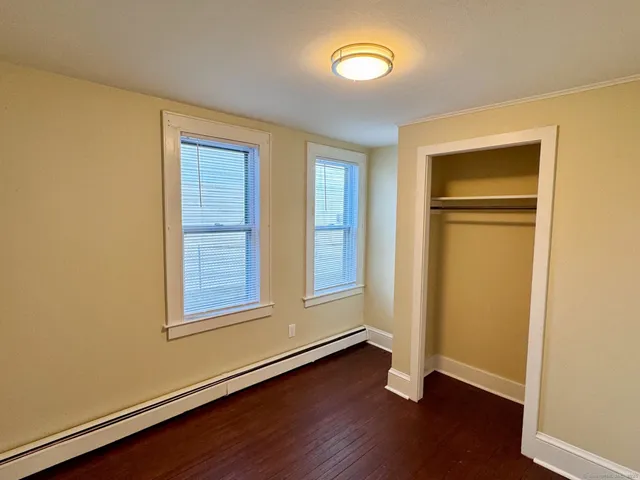 an empty room with wooden floor closet and windows
