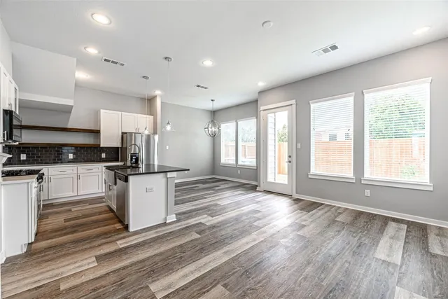 a open kitchen with granite countertop a stove top oven a sink and white cabinets with wooden floor