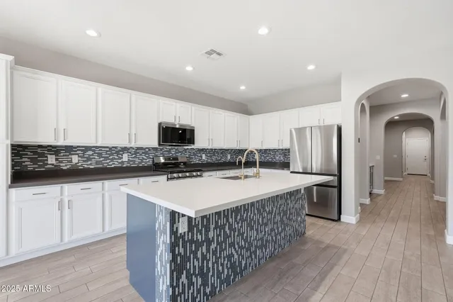 a large kitchen with stainless steel appliances a white stove top oven a refrigerator with white cabinets and wooden floor