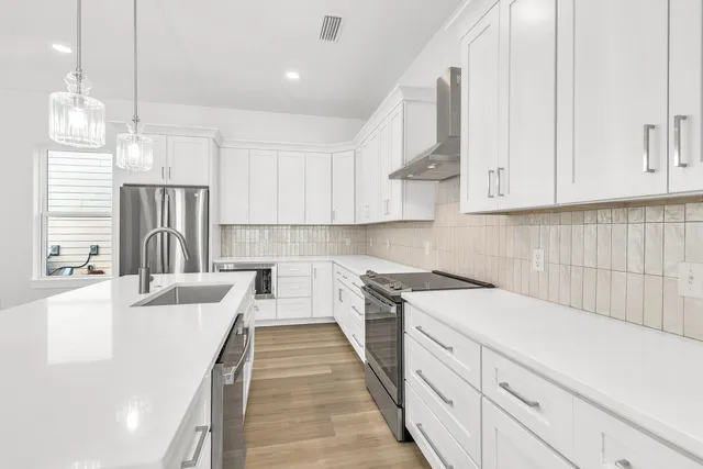 a kitchen with a sink dishwasher a stove a refrigerator and white cabinets with wooden floor