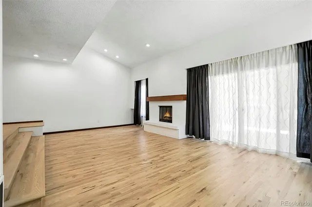 a view of an empty room with wooden floor and a kitchen