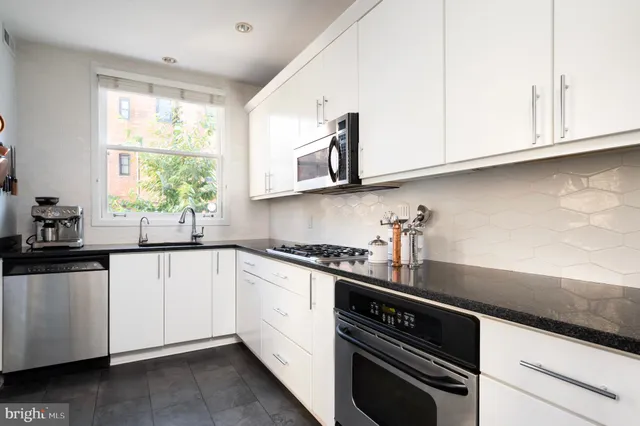 a kitchen with stainless steel appliances granite countertop white cabinets and a window
