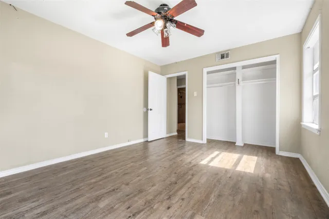 an empty room with wooden floor ceiling fan and windows