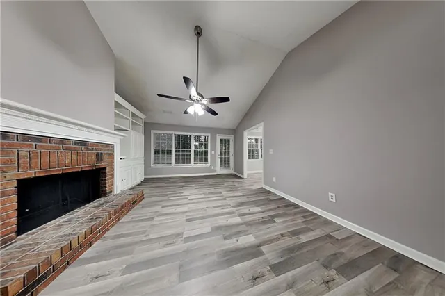 a view of an empty room with wooden floor fireplace and a window