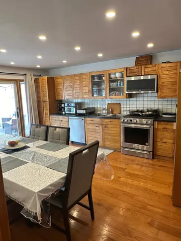 a kitchen with stainless steel appliances granite countertop a stove top oven a sink dishwasher a dining table and chairs with wooden floor