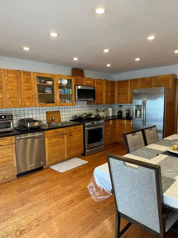 a kitchen with stainless steel appliances granite countertop a stove top oven a sink dishwasher a dining table and chairs with wooden floor