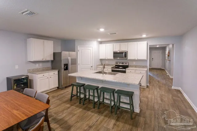 a kitchen with stainless steel appliances a stove a refrigerator a sink dishwasher and a dining table with wooden floor