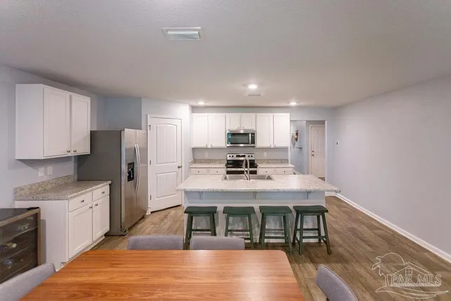 a kitchen with stainless steel appliances granite countertop a stove top oven a sink dishwasher and a refrigerator with wooden floor