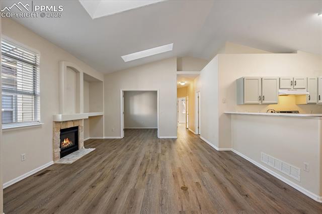 Unfurnished living room featuring a fireplace, dark wood-style flooring, vaulted ceiling, and a skylight