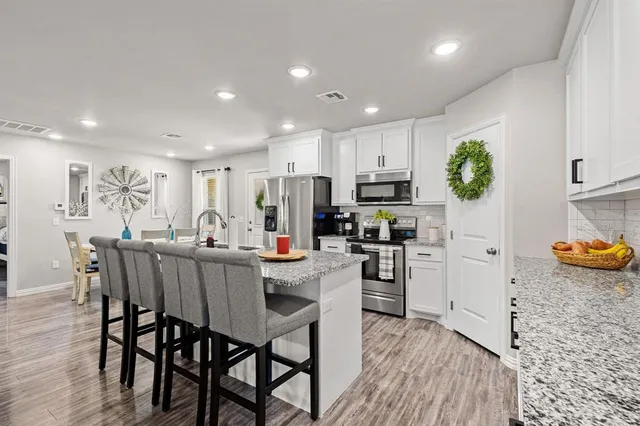 a kitchen with stainless steel appliances a dining table chairs stove refrigerator and cabinets