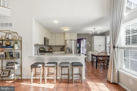 a large white kitchen with granite countertop a dining table chairs and a wooden floor