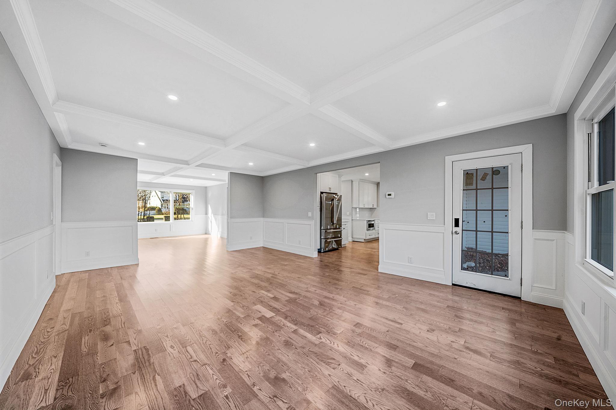 141 Wilmot Road Scarsdale, NY 10583 - Photo 11 of 49 Unfurnished living room with a wainscoted wall, light wood-type flooring, coffered ceiling, a decorative wall, and beam ceiling