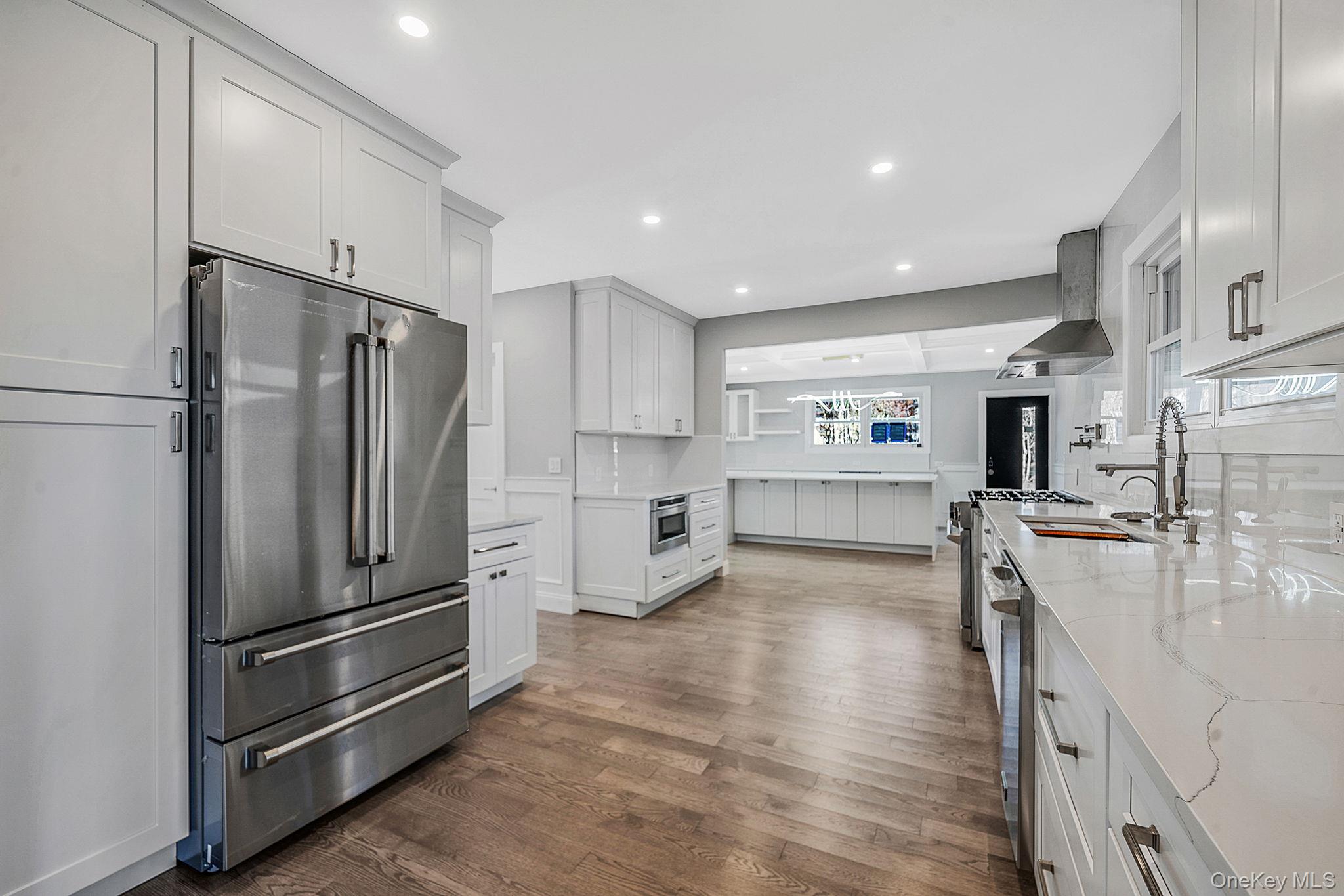 141 Wilmot Road Scarsdale, NY 10583 - Photo 12 of 49 Kitchen with stainless steel appliances, wall chimney exhaust hood, light stone counters, dark wood-type flooring, and white cabinetry