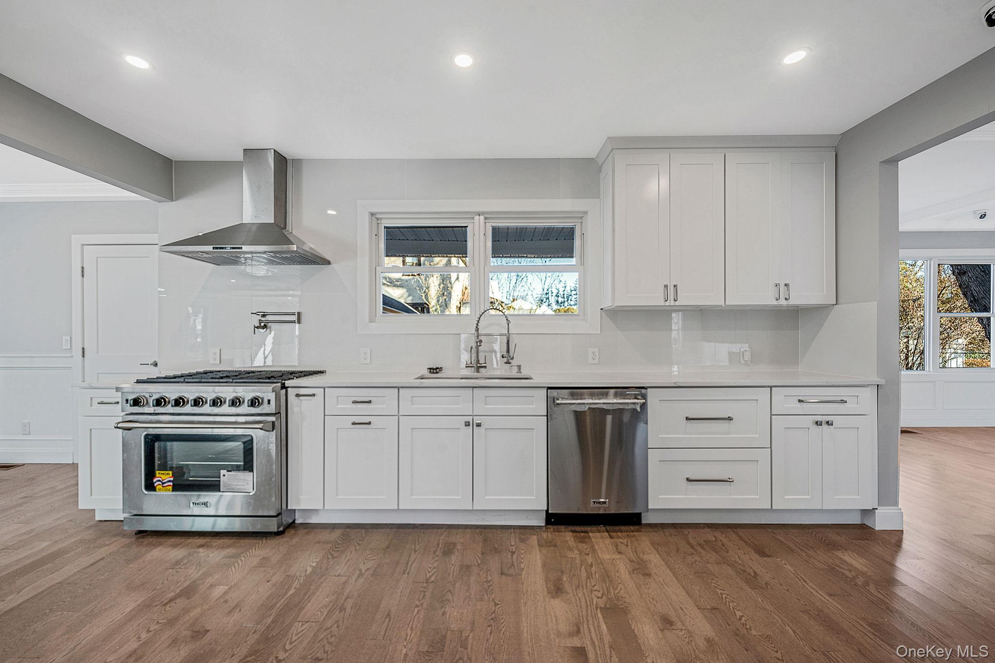 141 Wilmot Road Scarsdale, NY 10583 - Photo 13 of 49 Kitchen featuring appliances with stainless steel finishes, white cabinetry, wall chimney exhaust hood, dark wood-style flooring, and light stone countertops