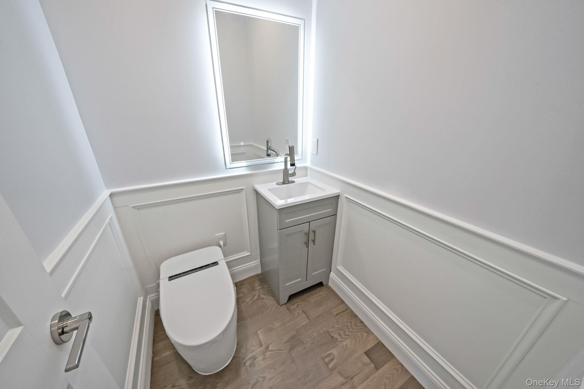 141 Wilmot Road Scarsdale, NY 10583 - Photo 29 of 49 Half bathroom with a decorative wall, vanity, wainscoting, and light wood-style flooring