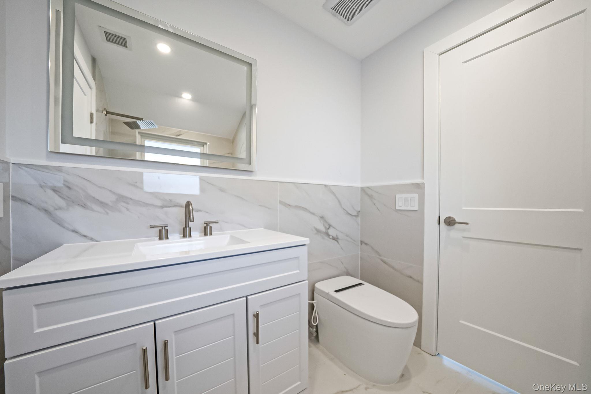 141 Wilmot Road Scarsdale, NY 10583 - Photo 30 of 49 Bathroom with vanity, tile walls, wainscoting, recessed lighting, and marble finish flooring