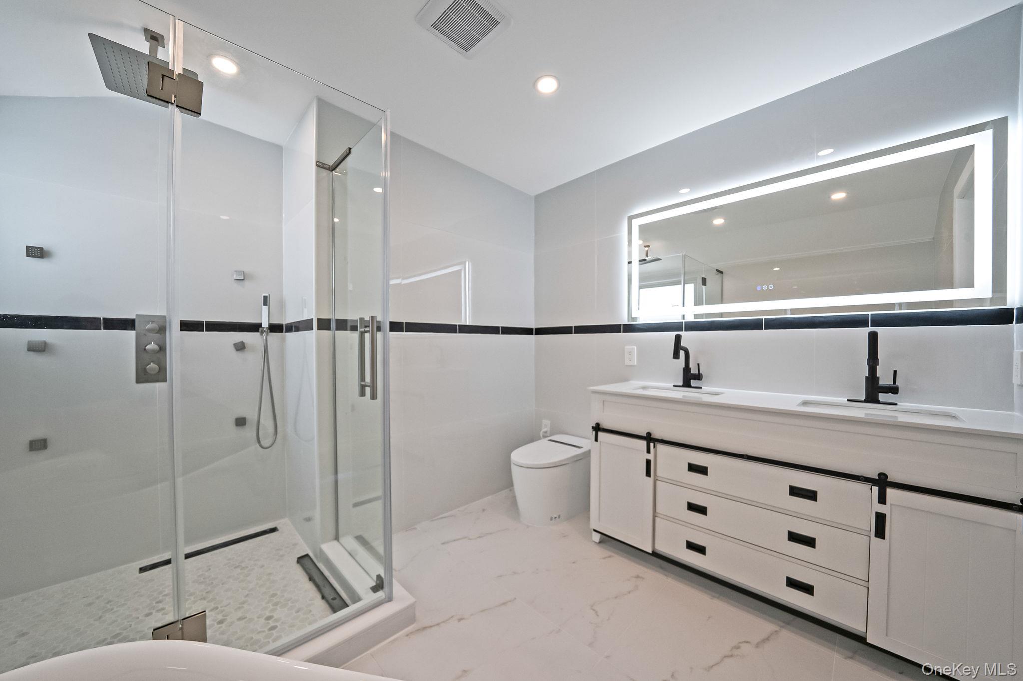 141 Wilmot Road Scarsdale, NY 10583 - Photo 33 of 49 Bathroom with double vanity, a shower stall, recessed lighting, light marble finish flooring, and tile walls