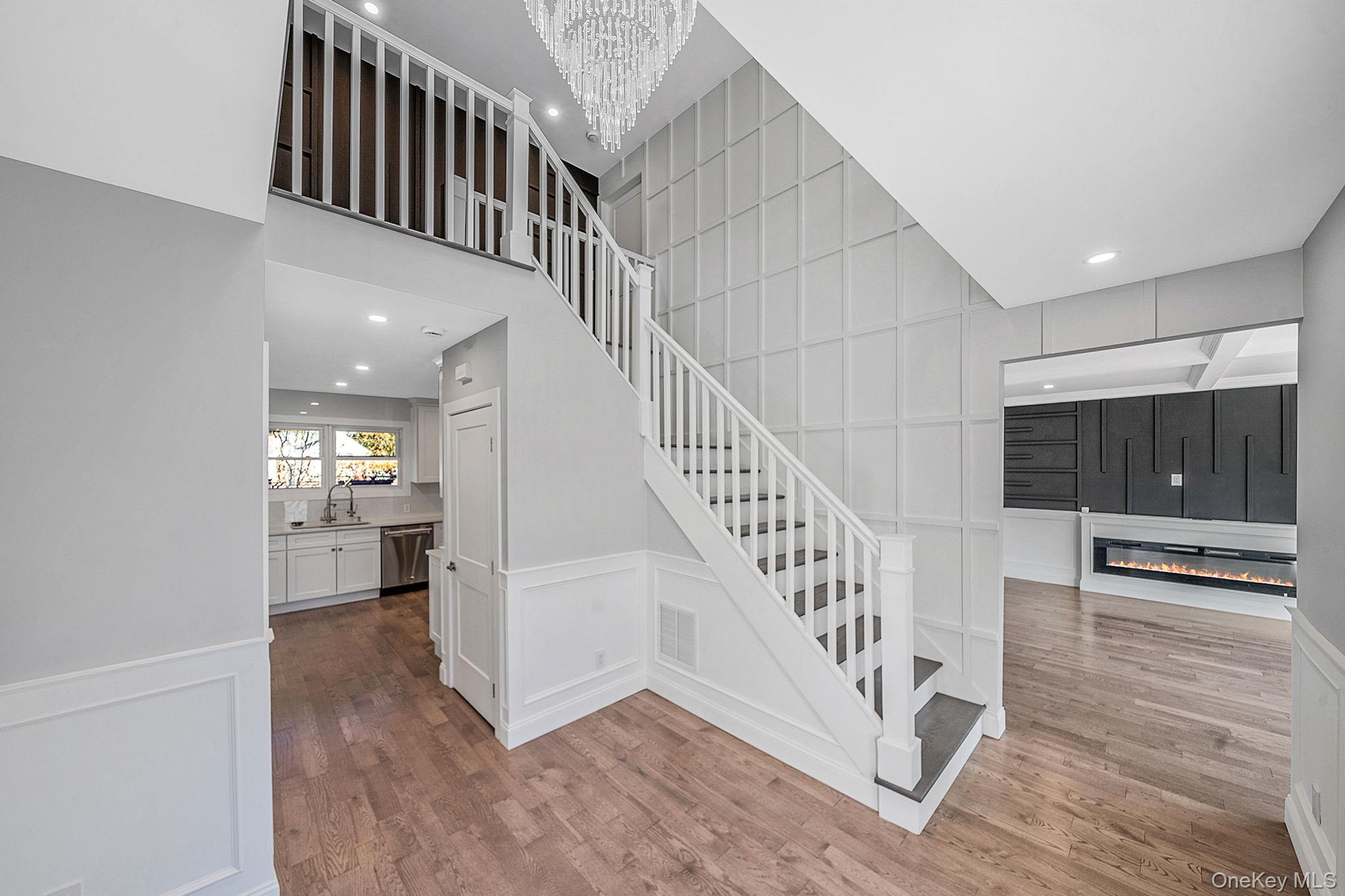 141 Wilmot Road Scarsdale, NY 10583 - Photo 4 of 49 Stairway with wood finished floors, a decorative wall, a chandelier, wainscoting, and a glass covered fireplace