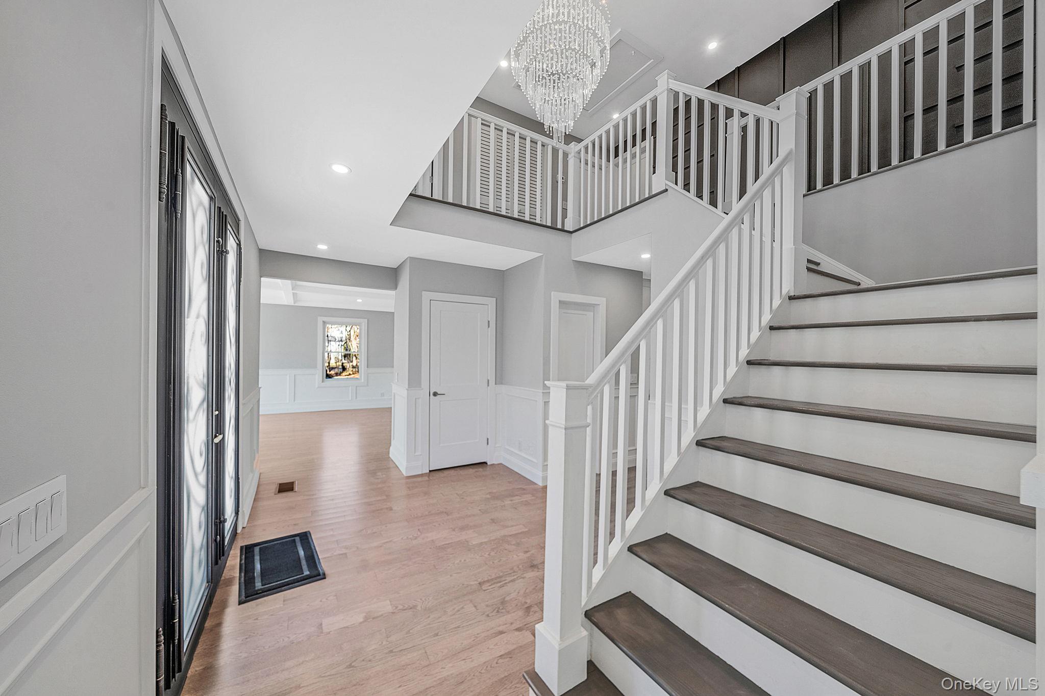 141 Wilmot Road Scarsdale, NY 10583 - Photo 5 of 49 Entrance foyer with a decorative wall, wainscoting, light wood finished floors, a chandelier, and stairs