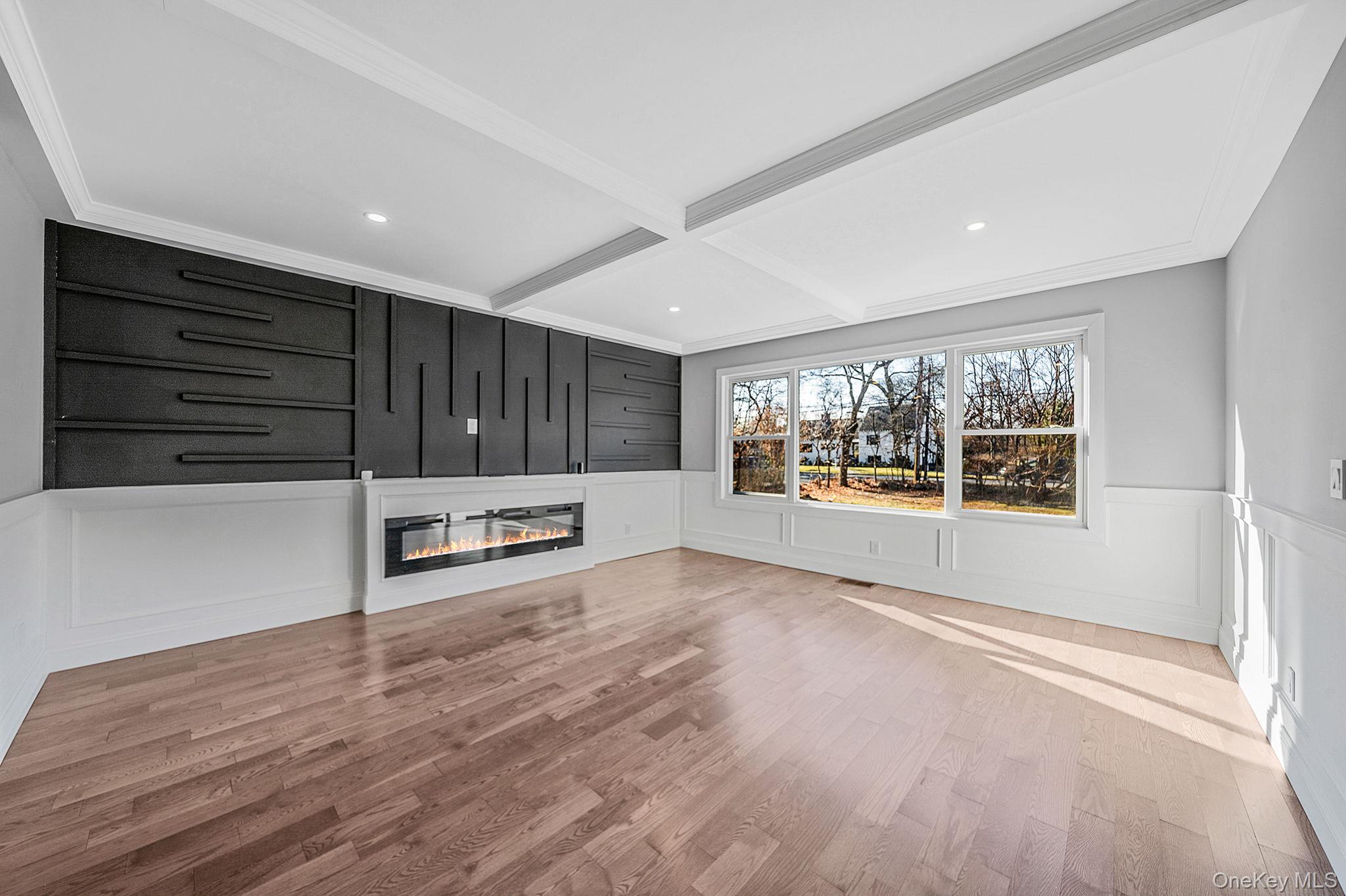 141 Wilmot Road Scarsdale, NY 10583 - Photo 6 of 49 Unfurnished living room featuring a decorative wall, a wainscoted wall, coffered ceiling, beamed ceiling, and light wood finished floors