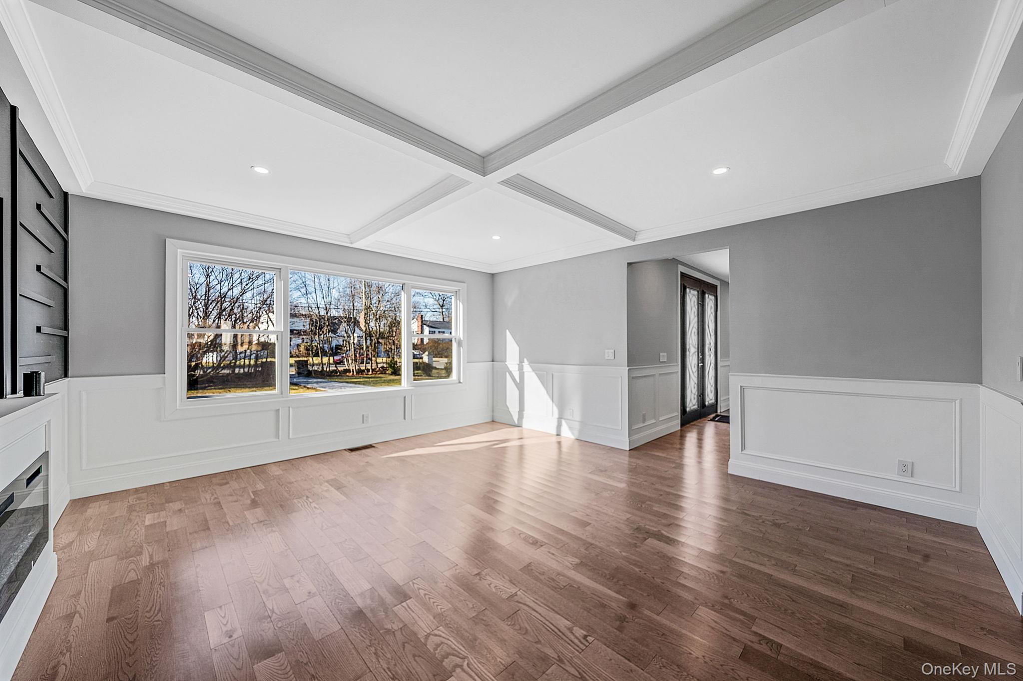 141 Wilmot Road Scarsdale, NY 10583 - Photo 7 of 49 Unfurnished living room with a wainscoted wall, wood finished floors, coffered ceiling, a decorative wall, and beamed ceiling
