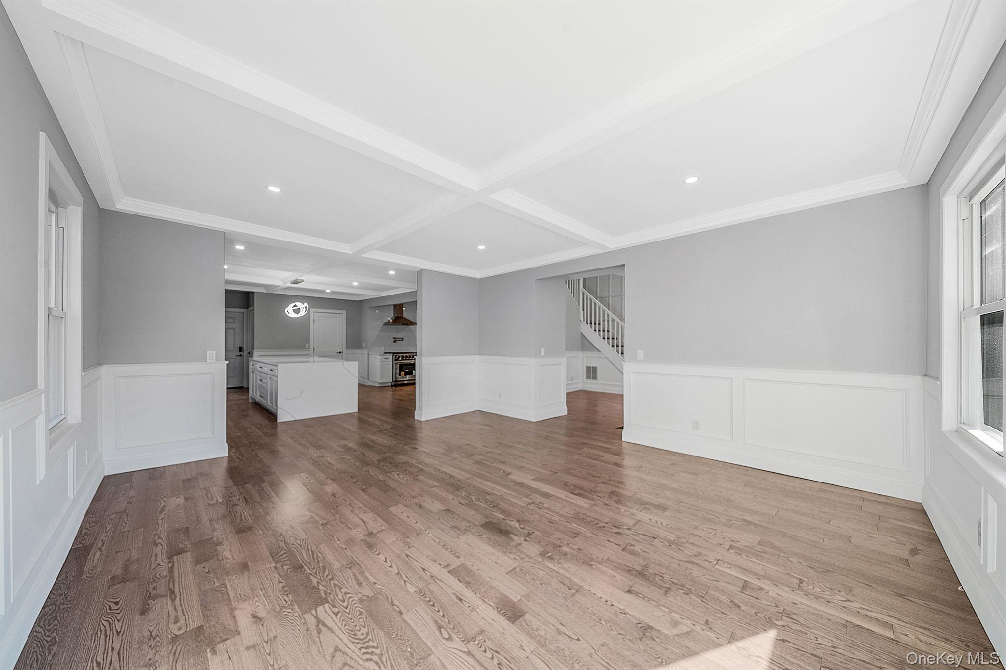 141 Wilmot Road Scarsdale, NY 10583 - Photo 9 of 49 Unfurnished living room featuring a wainscoted wall, a decorative wall, light wood-type flooring, beam ceiling, and stairs