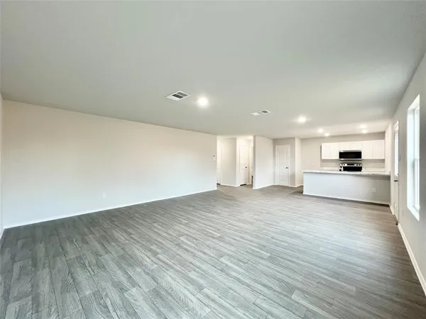 a view of empty room with wooden floor and kitchen view