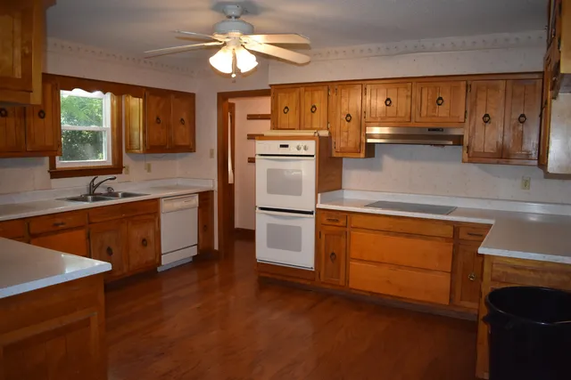 a kitchen with stainless steel appliances granite countertop a refrigerator a sink dishwasher a stove and white countertops with wooden floor