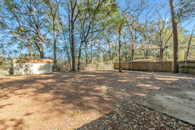 a backyard of a house with large trees and wooden fence