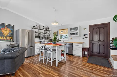 a kitchen with stainless steel appliances kitchen island granite countertop a refrigerator a stove top oven a dining table and chairs with wooden floor