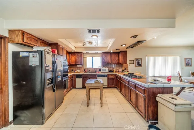 a kitchen with stainless steel appliances granite countertop a refrigerator a sink dishwasher a stove and a dining table with wooden floor