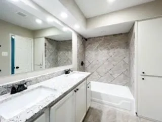 a bathroom with a granite countertop double vanity sink and a bathtub