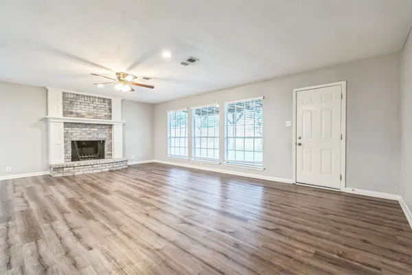 a view of an empty room with wooden floor fireplace and a window