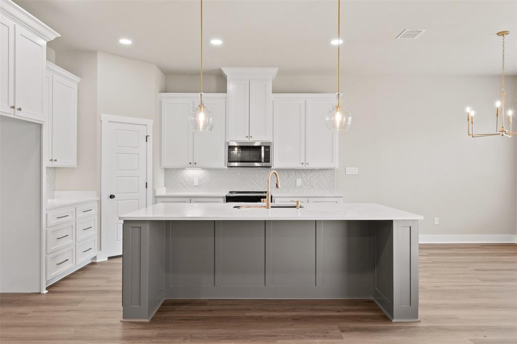 9824 Durango Trail Waco, TX 76712 - Photo 8 of 30 Modern kitchen featuring a spacious gray island with a white countertop, white cabinetry, brass pendant lighting, and wood-finish flooring