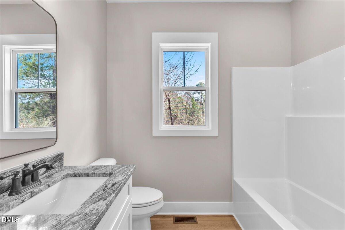 12615 Mallard Rock Drive Zebulon, NC 27597 - Photo 54 of 89 a bathroom with a granite countertop sink toilet a large mirror a bathtub and window