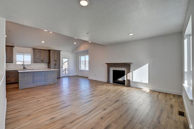1848 Mantle Way, Unit 417 Tooele, UT 84074 - Photo 3 of 6 Vaulted ceilings highlight this open-concept room featuring wood-finish flooring, a built-in fireplace with a decorative mantel, and recessed lighting