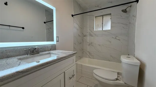 a bathroom with a granite countertop bathtub shower sink vanity and toilet