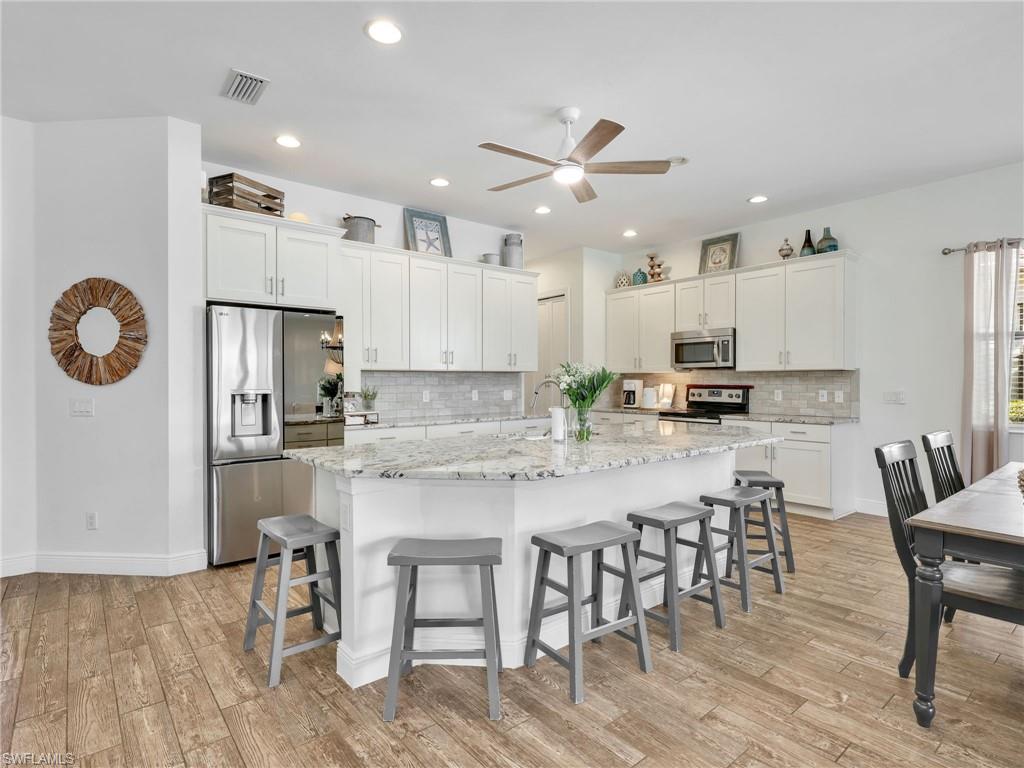 4743 Abaca Circle Naples, FL 34119 - Photo 13 of 50 Kitchen featuring appliances with stainless steel finishes, a large island with sink, light stone counters, white cabinets, and a breakfast bar