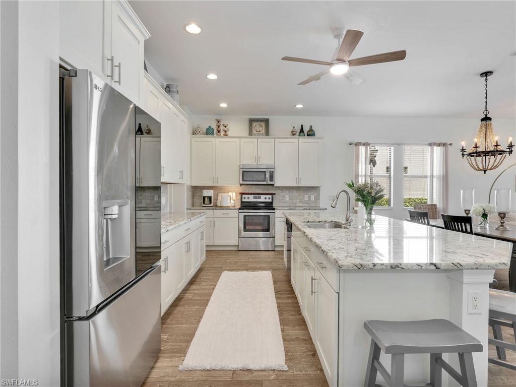 4743 Abaca Circle Naples, FL 34119 - Photo 16 of 50 Kitchen with appliances with stainless steel finishes, a kitchen bar, light stone counters, decorative backsplash, and an island with sink