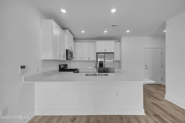 a kitchen with stainless steel appliances a sink a stove a refrigerator a white cabinets and a counter top